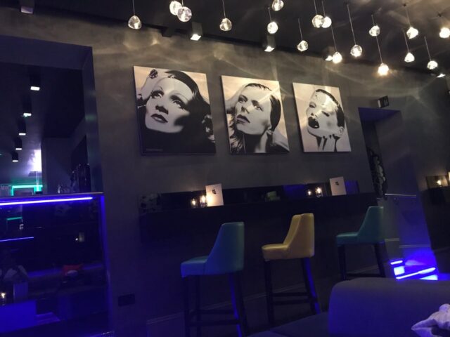 The Light Lounge gay bar interior. Three portraits hang above bar stools. Modern lighting. Gay travel advice.