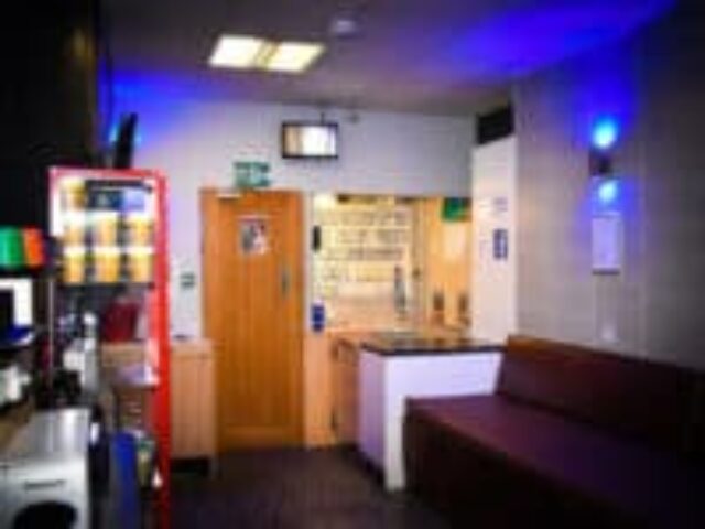 The Locker Room gay sauna interior. Features a vending machine, door, counter, and couch. Blue lighting adds to the ambiance.