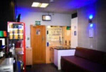 The Locker Room gay sauna interior. Features a vending machine, door, counter, and couch. Blue lighting adds to the ambiance.