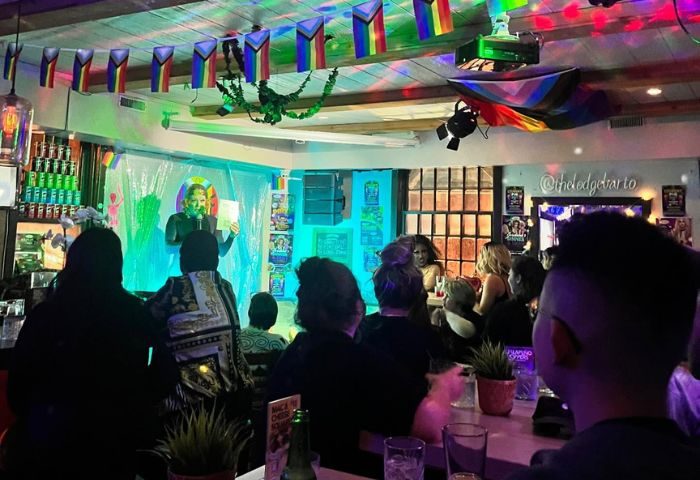 The Lodge at O'Gradys in Toronto. Gay bar with a drag queen performing on stage. Rainbow flags hang above the crowd. Gay travel.