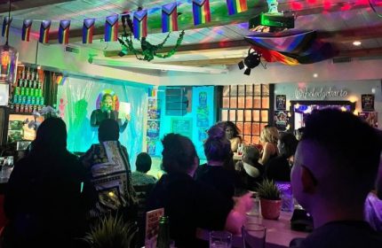 The Lodge at O'Gradys in Toronto. Gay bar with a drag queen performing on stage. Rainbow flags hang above the crowd. Gay travel.