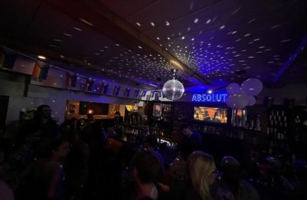 Inside The Lodge at O'Gradys gay bar in Toronto. Disco ball, rainbow flags, & Absolut sign. Gay travel advice for men.