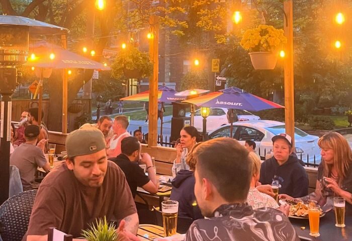 The Lodge at O'Grady's in Toronto: Outdoor patio scene with gay men enjoying drinks and food under string lights and rainbow umbrellas.