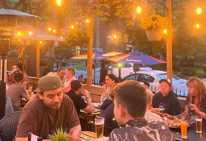 The Lodge at O'Grady's in Toronto: Outdoor patio scene with gay men enjoying drinks and food under string lights and rainbow umbrellas.