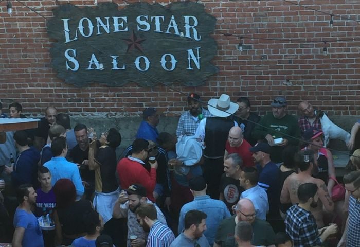 Lone Star Saloon in San Francisco: A lively outdoor gathering of gay men at the popular bar, with a brick wall and the saloon's sign.