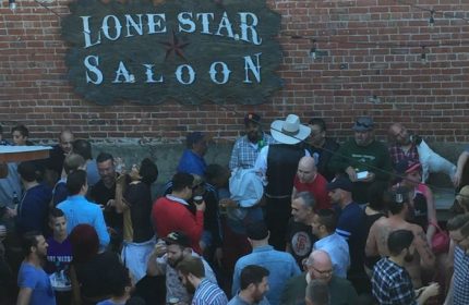 Lone Star Saloon in San Francisco: A lively outdoor gathering of gay men at the popular bar, with a brick wall and the saloon's sign.