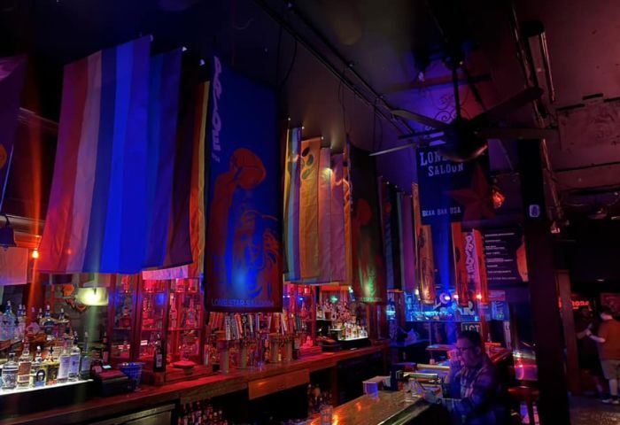 Interior of The Lone Star Saloon, San Francisco, a gay bar. Rainbow flags and banners hang above the bar. A man sits at the counter.
