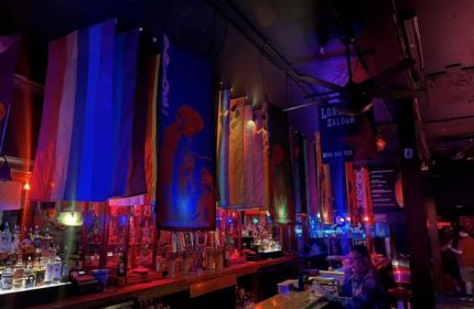 Interior of The Lone Star Saloon, San Francisco, a gay bar. Rainbow flags and banners hang above the bar. A man sits at the counter.