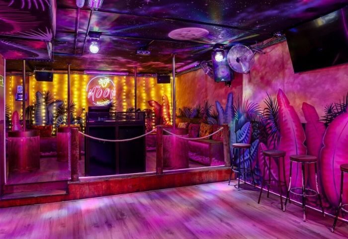 Interior of The Moon Tropical Gay Club in Madrid. Tropical decor, neon sign, DJ booth, and vibrant lighting create a fun atmosphere.