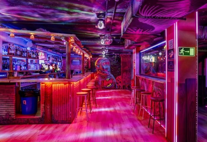 Interior of The Moon Tropical Gay Club in Madrid. Pink lighting, bar stools, and a mural of a monkey astronaut. Gay travel.