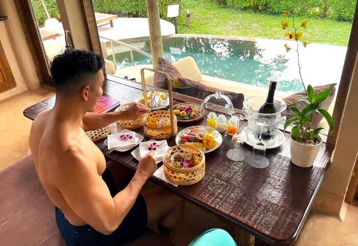 Gay man enjoys breakfast at The Naka Island, a Luxury Collection Resort & Spa, Phuket. Beachfront pool villa with wine and fruit.