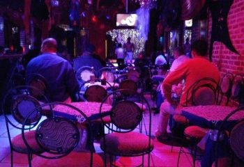 Interior of The New Jalisco Bar, a gay bar. Men sit at tables, with shirtless dancers on stage. Jalisco bar nightlife.