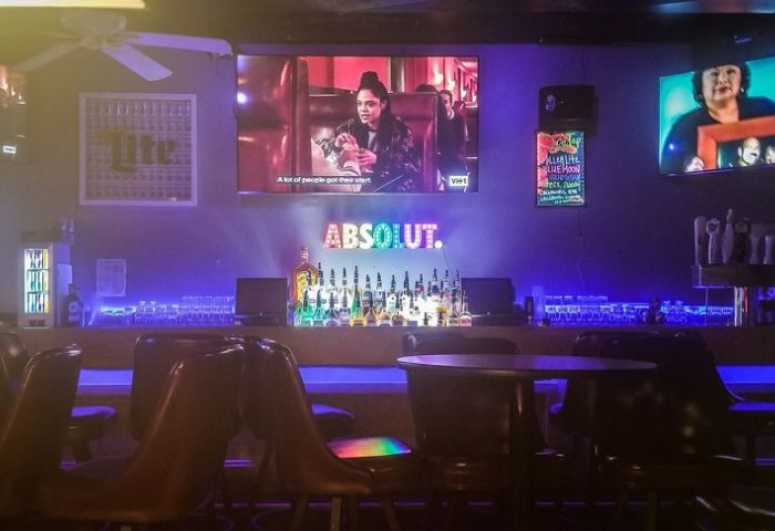 Interior of The North End gay sports bar in Chicago. TVs, bar with liquor, Absolut sign, blue lighting. Gay travel advice.