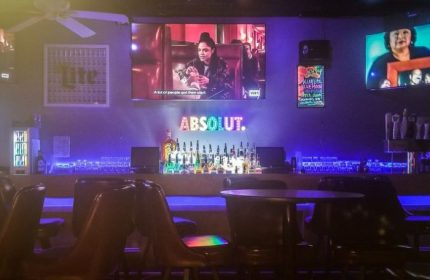 Interior of The North End gay sports bar in Chicago. TVs, bar with liquor, Absolut sign, blue lighting. Gay travel advice.