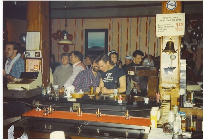 Vintage photo of The North End gay sports bar in Chicago. Men at the bar, cocktail hour sign, and festive decor. Gay travel.