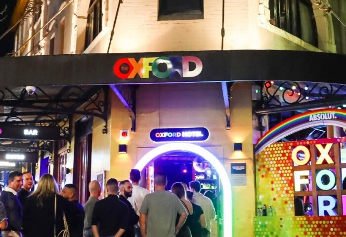 The Oxford Hotel Sydney entrance at night. Gay bar with rainbow colors, people, and vibrant lighting. Gay travel advice in Sydney.
