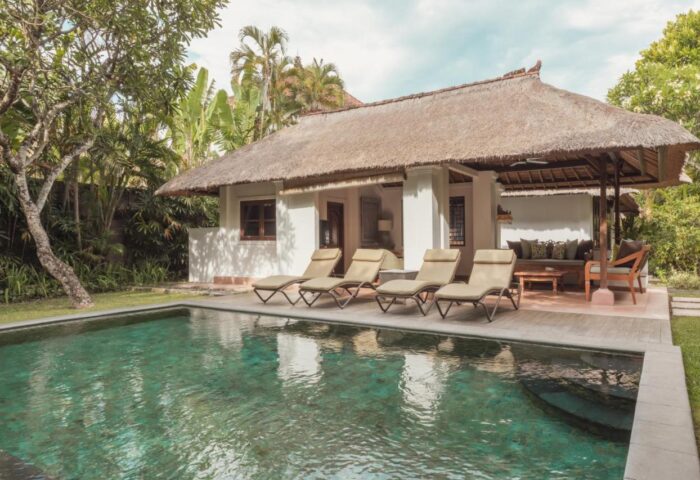 The Pavilions Bali gay-friendly hotel. Thatched roof villa with pool, lounge chairs, and outdoor seating for a relaxing gay travel experience.