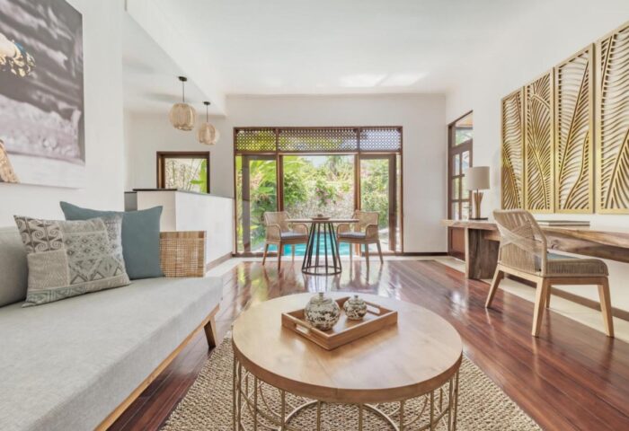The Pavilions Bali gay-friendly hotel interior. Living area with sofa, table, desk, and view to the pool. Luxury travel for gay men in Bali.