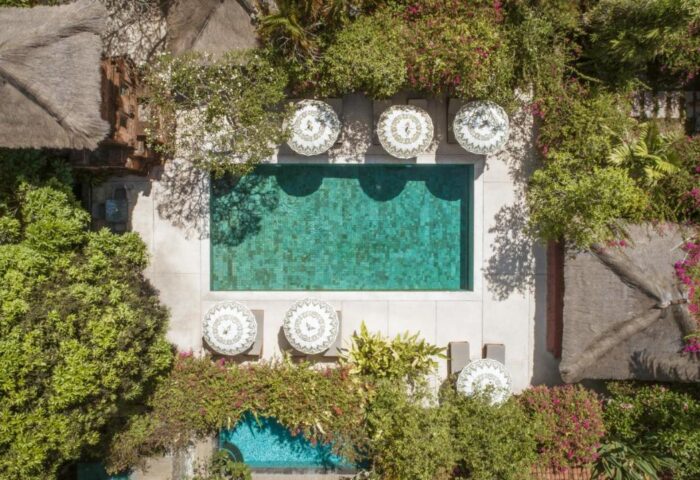Aerial view of The Pavilions Bali gay-friendly hotel. Lush greenery surrounds a pool with parasols. Tropical paradise for gay travel.