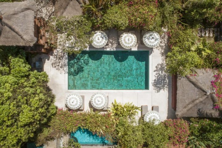 Aerial view of The Pavilions Bali gay-friendly hotel. Lush greenery surrounds a pool with parasols. Tropical paradise for gay travel.
