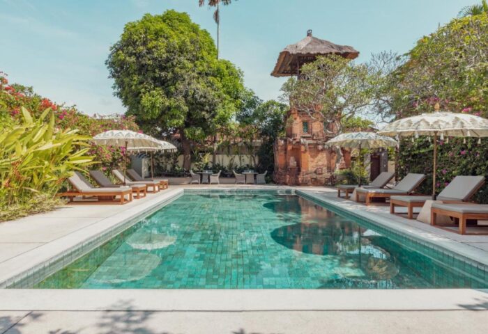 The Pavilions Bali gay-friendly hotel pool. Lush greenery, lounge chairs, and parasols surround the turquoise pool. A serene Bali getaway.