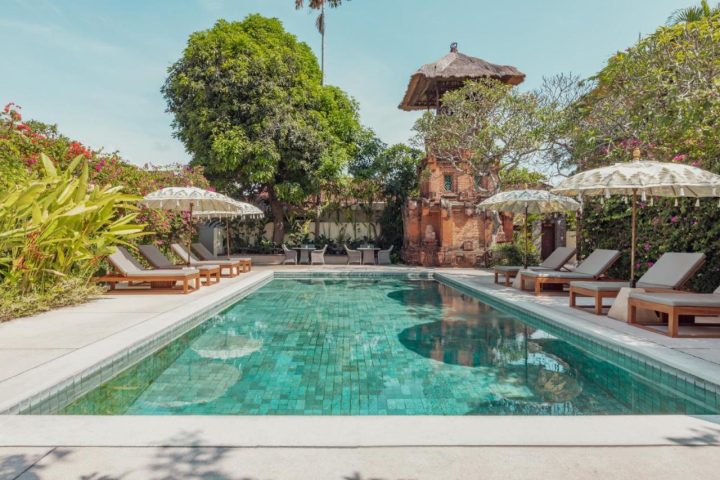 The Pavilions Bali gay-friendly hotel pool. Lush greenery, lounge chairs, and parasols surround the turquoise pool. A serene Bali getaway.