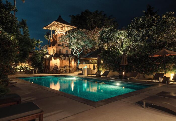 The Pavilions Bali gay-friendly hotel pool at night. Lounge chairs surround the pool. A Balinese tower is in the background.