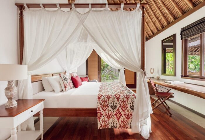 The Pavilions Bali gay-friendly hotel room. Four-poster bed with white curtains, desk, & wood floors create a luxurious, romantic vibe.