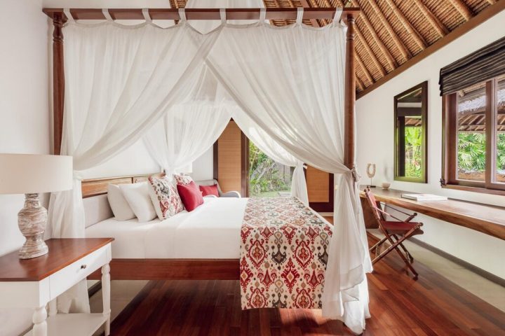 The Pavilions Bali gay-friendly hotel room. Four-poster bed with white curtains, desk, & wood floors create a luxurious, romantic vibe.
