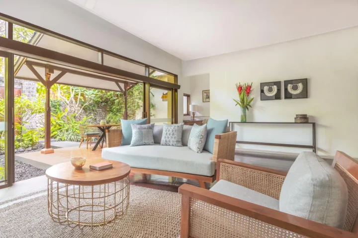 Living area at The Pavilions Bali, a gay-friendly hotel. Features stylish seating, a coffee table, and a view of the lush outdoor space.