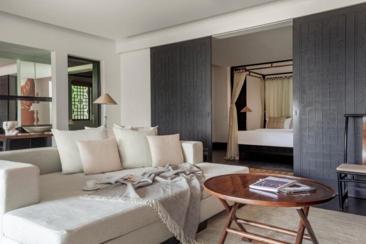 The Pavilions Phuket suite living area. Gay Phuket travel. Luxury hotel room with sofa, coffee table, and bedroom view. Stylish design.