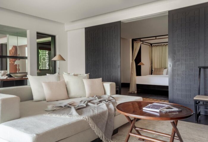 The Pavilions Phuket suite living area. Gay Phuket travel. Luxury hotel room with sofa, coffee table, and bedroom view. Stylish design.