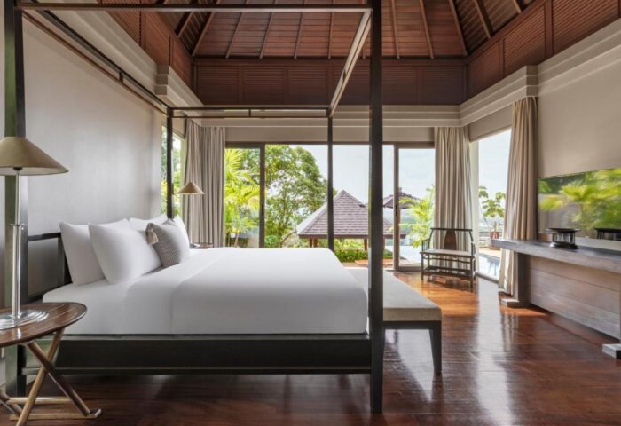 The Pavilions Phuket suite. Gay Phuket travel. Four-poster bed, wood floors, and a view of the pool. Luxury gay travel in Thailand.
