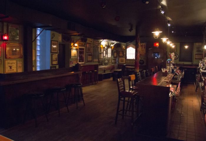 Interior of The Phoenix Gay Bar in New York. Bar stools line the counter. Walls are adorned with pictures. Dark lighting. Gay travel.
