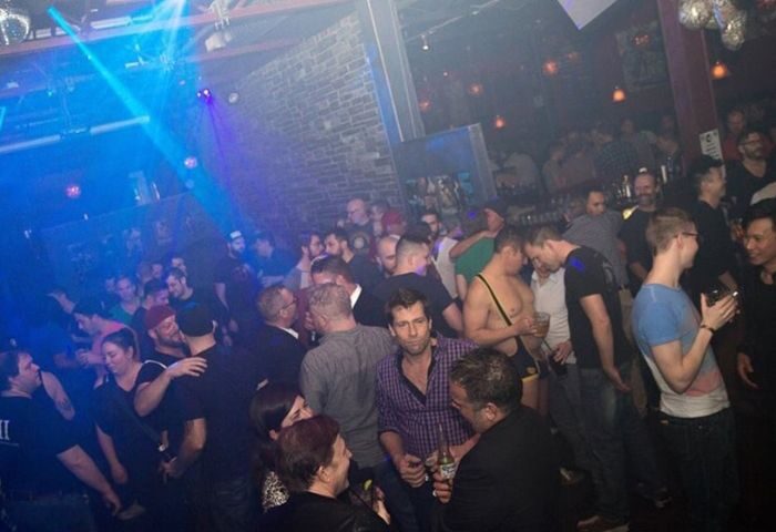 Inside Vancouver's Pumpjack Pub, a popular gay bar. A diverse crowd of men mingle under blue lighting, enjoying drinks and socializing. Gay travel advice.