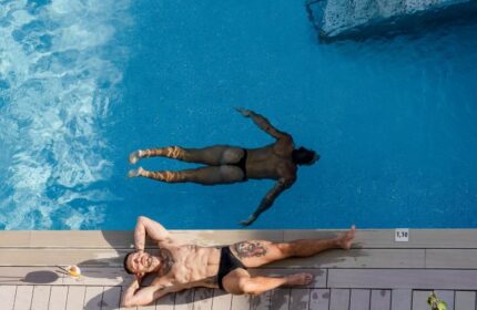 Two gay men at The Purple Hotel, Ibiza. One swims in the pool, the other sunbathes poolside. Gays-only travel destination.