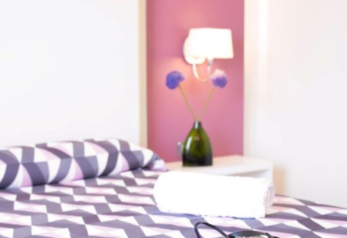Purple Hotel Ibiza room: Bed with briefs and camera. Gay travel lodging with purple accents, modern design, and amenities.