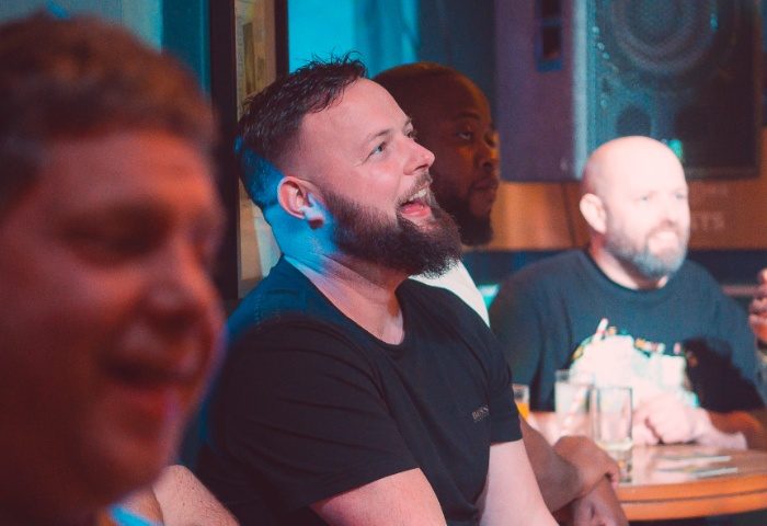 Gay men at The Rem Bar, Manchester. Bearded man smiling, with friends. Gay travel advice, nightlife, and bar scene.