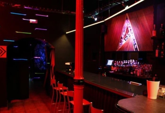 Interior of The Ring, a private gay cruise club in Madrid. Red lighting, bar with bottles, and a dance floor area. Gay nightlife travel.