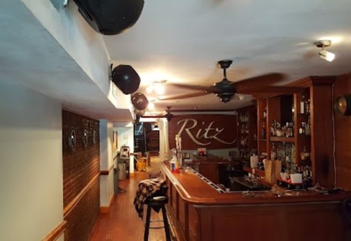 Interior of The Ritz Bar and Lounge in New York. Bar with liquor bottles, fans, and the Ritz logo. Gay travel destination.