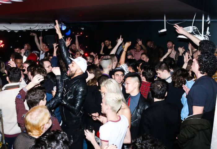 Packed crowd at The Rosemont, a chill gay bar in New York City. People dancing, raising hands, enjoying the nightlife scene.