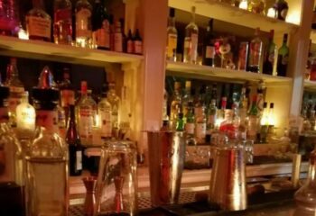 The Rosemont Chill, a gay bar in New York. Shelves of liquor bottles behind a bar with shakers and glassware. Gay travel advice.