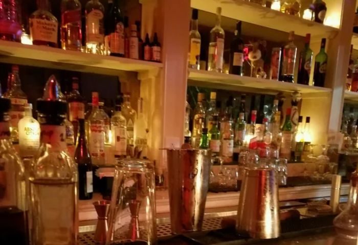 The Rosemont Chill, a gay bar in New York. Shelves of liquor bottles behind a bar with shakers and glassware. Gay travel advice.