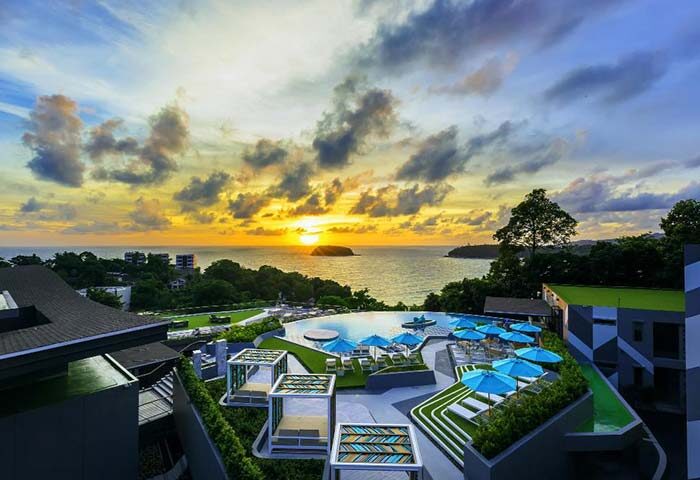 The SIS Kata Resort gay hotel sunset view. Pool with blue umbrellas overlooking the ocean. Kata, Phuket, Thailand. Gay travel.