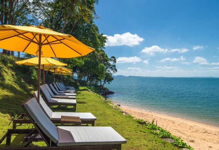 The Shell Sea Krabi beachfront. Chic gay hotel with beach chairs and yellow umbrellas on the lawn. Perfect for gay travel advice.