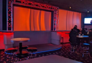 Interior of The Silver Fox dancefloor, a gay bar. Stage with red lighting, tables with stools, and patrons. Gay travel advice.