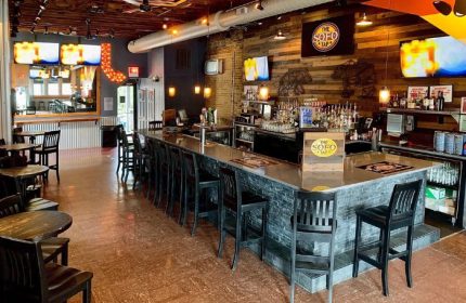 Interior of The SoFo Tap, a gay bear bar in Chicago. Long bar with stools, tables, TVs, and a rustic wood wall. Gay travel advice.