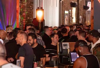 Crowded scene inside The SoFo Tap, a popular gay bear bar in Chicago. Men are socializing at the bar, enjoying the lively atmosphere.