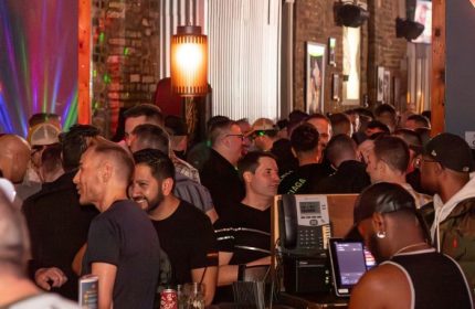 Crowded scene inside The SoFo Tap, a popular gay bear bar in Chicago. Men are socializing at the bar, enjoying the lively atmosphere.