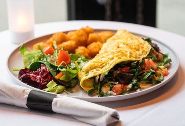 The Spot in New York: Omelet with tater tots and salad on a plate. Gay travel-friendly dining experience in NYC.